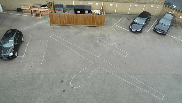 Drone Shadows, image of a car park with the drawing of a drone on the ground