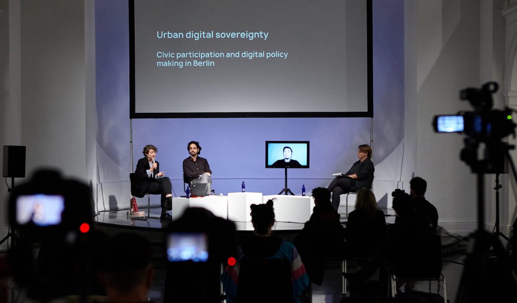 Panel discussion “Citizens for Digital Sovereignty: Shaping Inclusive & Resilient Cities” with Elizabeth Calderón Lüning (left), Rafael Heiber, Alexandre Monnin (screen), and Lieke Ploeger.